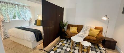 Un dormitorio moderno con cama, mesita de noche y sofá con alfombra estampada.