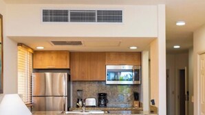 A compact kitchen with wooden cabinets, stainless steel appliances, and a bar stool seating area.