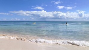 Ein Strand mit klarem, blauem Wasser, einem sandigen Ufer und einer Person, die surft.