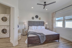 Un dormitorio con cama, ventilador de techo, lavadora y ventana con cortinas.