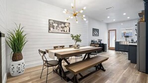 A modern kitchen with white cabinetry, a wooden dining table with benches, and a hanging light fixture. - Paso Robles Bungalow -Deck/Fire Pit (Paso Robles)