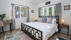 A bedroom with a bed, two bedside tables, a desk, a chair, a ceiling fan, and a window with curtains. - Paso Robles Bungalow -Deck/Fire Pit (Paso Robles)