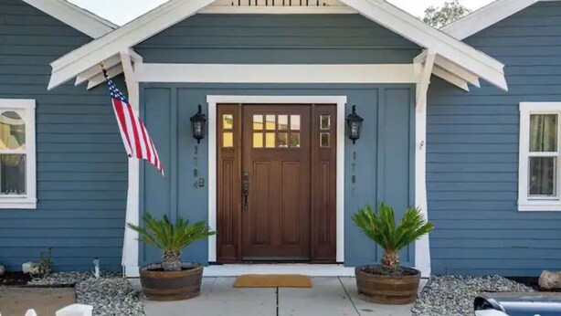 A house with a blue exterior, a brown front door, two potted plants, an American flag, and a white picket fence. - Paso Robles Bungalow -Deck/Fire Pit (Paso Robles)