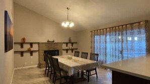 Uma sala de jantar com uma mesa, cadeiras, um candelabro e uma janela com cortinas.