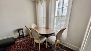A dining area with a round table, four chairs, a small side table, and a patterned rug.