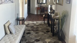 A spacious living room with a wooden floor, a white sofa, a coffee table, and a rug. There is a ceiling fan, a mirror, and artwork on the walls.