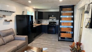 A modern kitchen with dark cabinets, a black refrigerator, and a wooden staircase leading to an upper level. - The Archer House - 1 Block from Spring River.  2 Bedrooms + Loft Bedroom!   (Mammoth Spring)