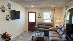 A living room with a brown leather sofa, a coffee table, a TV mounted on the wall, and a door leading to another room. - The Archer House - 1 Block from Spring River.  2 Bedrooms + Loft Bedroom!   (Mammoth Spring)