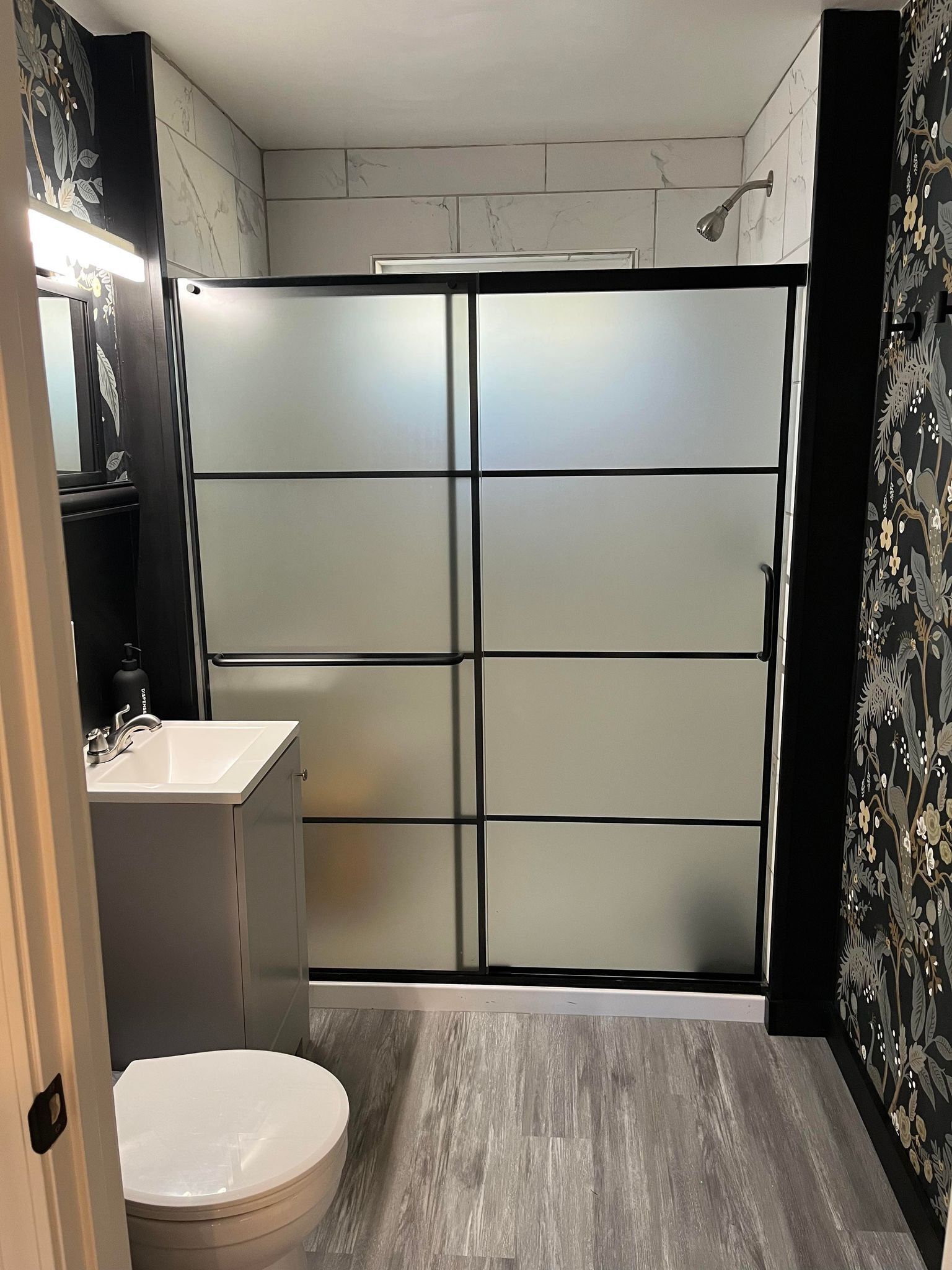 A bathroom with a modern design, featuring a toilet, sink, and a shower area with frosted glass doors.