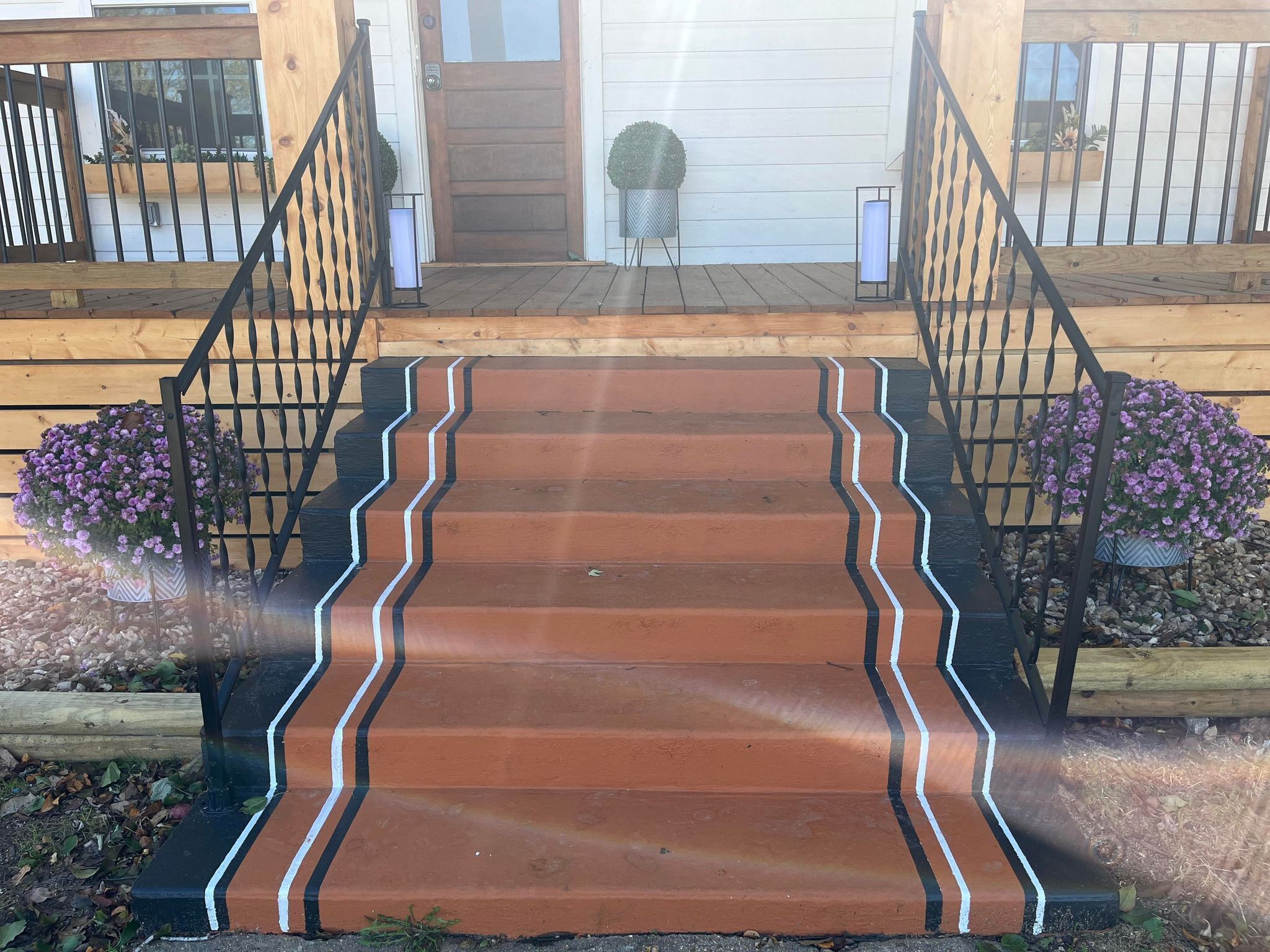 Un escalier en bois menant à l’entrée d’une maison, avec une rampe en métal.