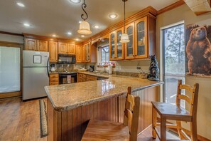 Una cocina con armarios de madera, encimeras de granito, un refrigerador de acero inoxidable y un mural de un oso.
