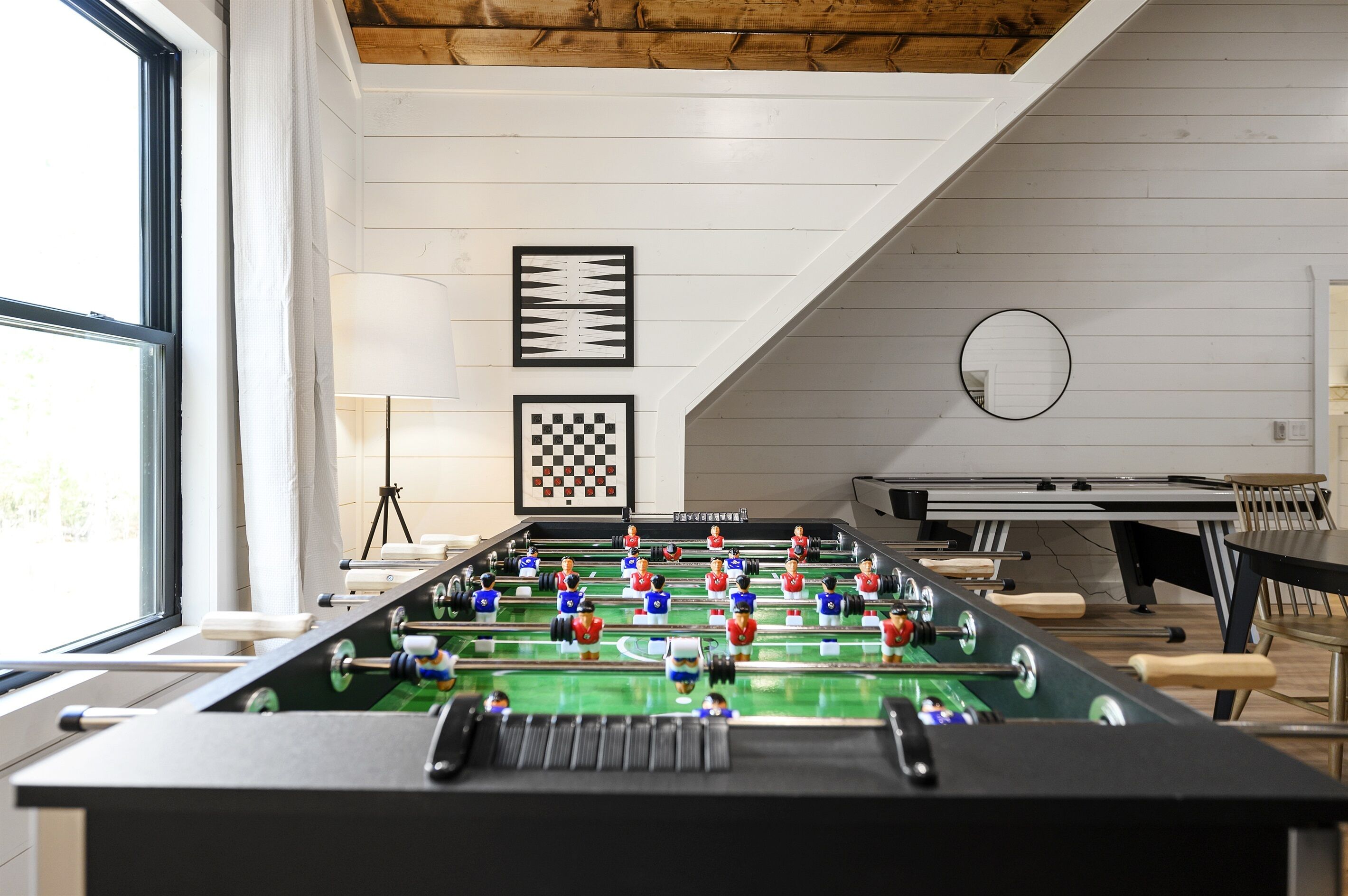 Une table de baby-foot dans une pièce aux murs blancs, avec un plafond en bois et une fenêtre.