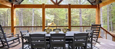 A wooden deck with a table and chairs, surrounded by a forest.