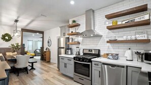 A modern kitchen with stainless steel appliances, wooden shelves, and a white tiled backsplash. - Paso Robles Retreat - Newly Remodeled- (Paso Robles)