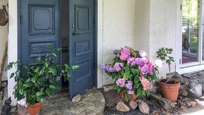 A blue door with decorative panels, two potted plants with hydrangeas, and a stone pathway leading to a window. - Beautiful home in Nybrostrand with WiFi (Nybrostrand)
