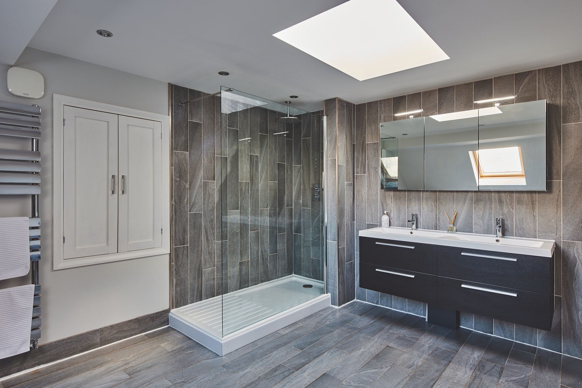 A modern bathroom with a glass-enclosed shower, a vanity with a mirror, and a skylight.