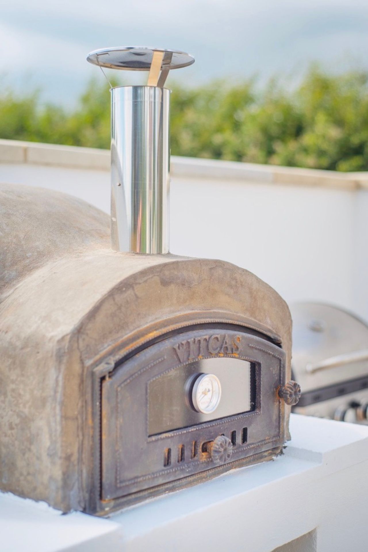 Una parrilla Vintcas antigua con una chimenea de metal, sobre una superficie blanca y un fondo verde desenfocado.
