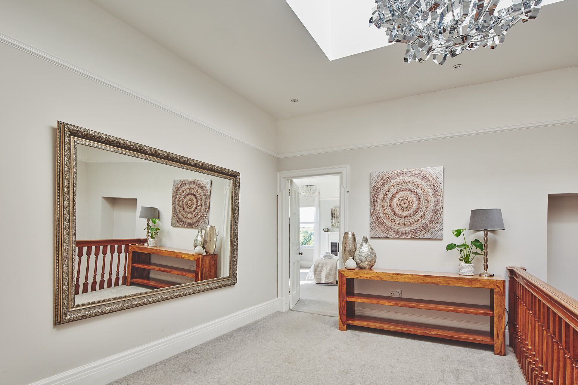 A spacious hallway with a large mirror, wooden console table, and two wall-mounted artworks.
