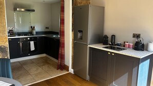 Een moderne keuken met donkere kastjes, een roestvrijstalen koelkast en een aanrecht met een waterkoker en kopjes.