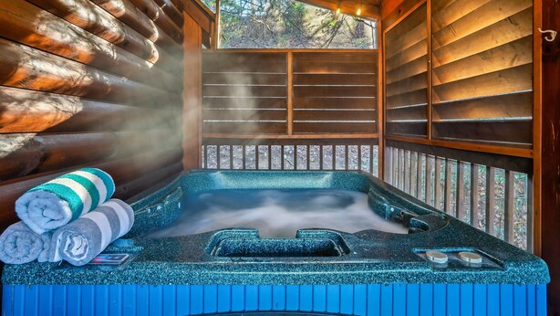 Un jacuzzi con vapor ascendiendo, rodeado de paredes de madera y una ventana con vista a árboles.