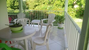 Ein Balkon mit weißen Plastikstühlen und einem Tisch, einem Topfpflanzen und Blick auf einen üppigen Garten.