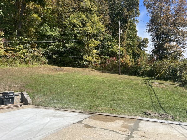 A backyard with a lawn, a barbecue grill, and a stone wall.