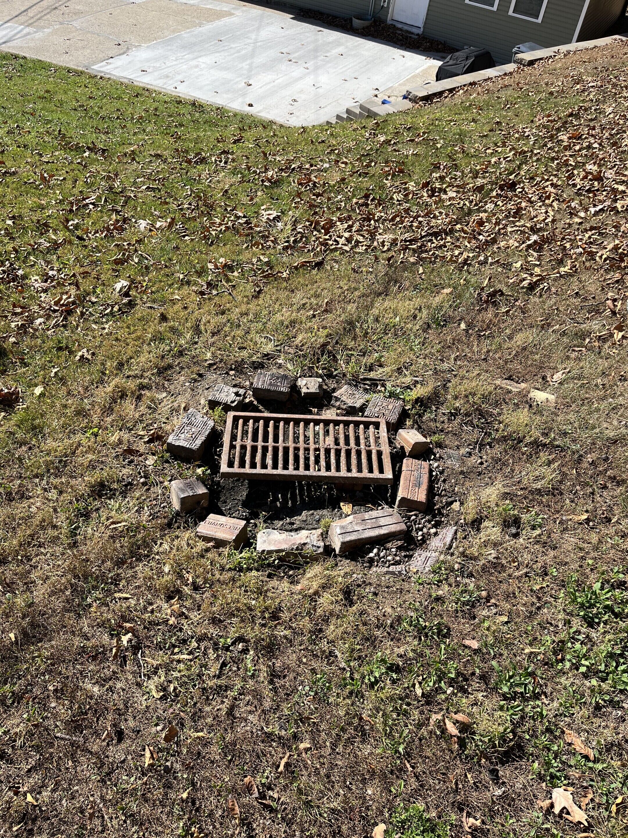 A grassy area with a manhole cover surrounded by bricks and stones.