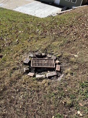 A grassy area with a manhole cover surrounded by bricks and stones.