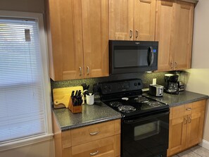A kitchen with wooden cabinets, a black microwave, a stove, and a coffee maker.
