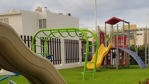 A playground with slides and climbing structures, surrounded by a well-maintained lawn and flower beds. - CASA ROBLE by TRVL2HM (Nuevo Nayarit)