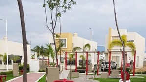An outdoor fitness area with exercise equipment, surrounded by a well-maintained lawn and trees. - CASA ROBLE by TRVL2HM (Nuevo Nayarit)