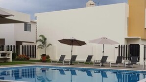 A swimming pool with lounge chairs and umbrellas, surrounded by modern buildings. - CASA ROBLE by TRVL2HM (Nuevo Nayarit)