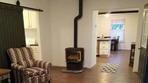 A living room with a patterned armchair, a sofa, a small table, and a wood-burning stove. - Quiet Private Country Cottage (Riverton)