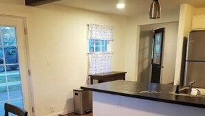A modern kitchen with a dark countertop, a built-in oven, and a refrigerator. There is a dining area with a wooden table and chairs. - Quiet Private Country Cottage (Riverton)