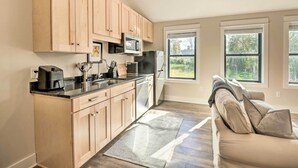Cocina moderna con armarios de madera, microondas, cafetera y refrigerador. Hay una ventana que proporciona luz natural y vistas al exterior.