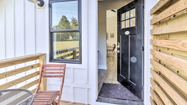 Una terraza de madera con una silla y una mesa, una puerta negra con ventanal, y un cartel de bienvenida.