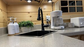 Eine Küche mit einem schwarzen Spülbecken, einer Kaffeemaschine und zwei Seifenflaschen auf der Arbeitsfläche.