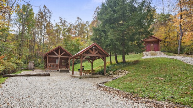 Eine rustikale Holzhütte mit Veranda und Picknicktisch, umgeben von einem Schotterweg und einer Rasenfläche.