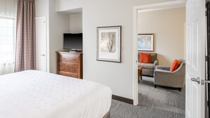 A hotel room with a large bed, a TV on a wooden dresser, a framed picture on the wall, and a seating area with a chair and a sofa.