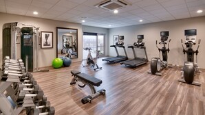Une salle de sport équipée de tapis de course, de vélos elliptiques, d’un banc et de matériel de musculation.