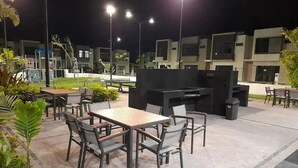An outdoor patio area with tables and chairs, a barbecue grill, and modern buildings in the background. - CASA VELA by TRVL2HM (Nuevo Nayarit)