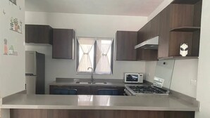 A modern kitchen with dark wooden cabinets, a central island with seating, a built-in microwave, and a gas stove. - CASA VELA by TRVL2HM (Nuevo Nayarit)