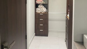 A walk-in closet with a dark wooden door, a white tiled floor, and a built-in shelving unit with folded clothes. - CASA VELA by TRVL2HM (Nuevo Nayarit)