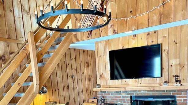 A cozy living room with a wooden staircase, a fireplace, a flat-screen TV, and a round coffee table with decorative items. - Enjoy Fall Foliage in Renov End Unit Townhouse with Fireplace (Dover)