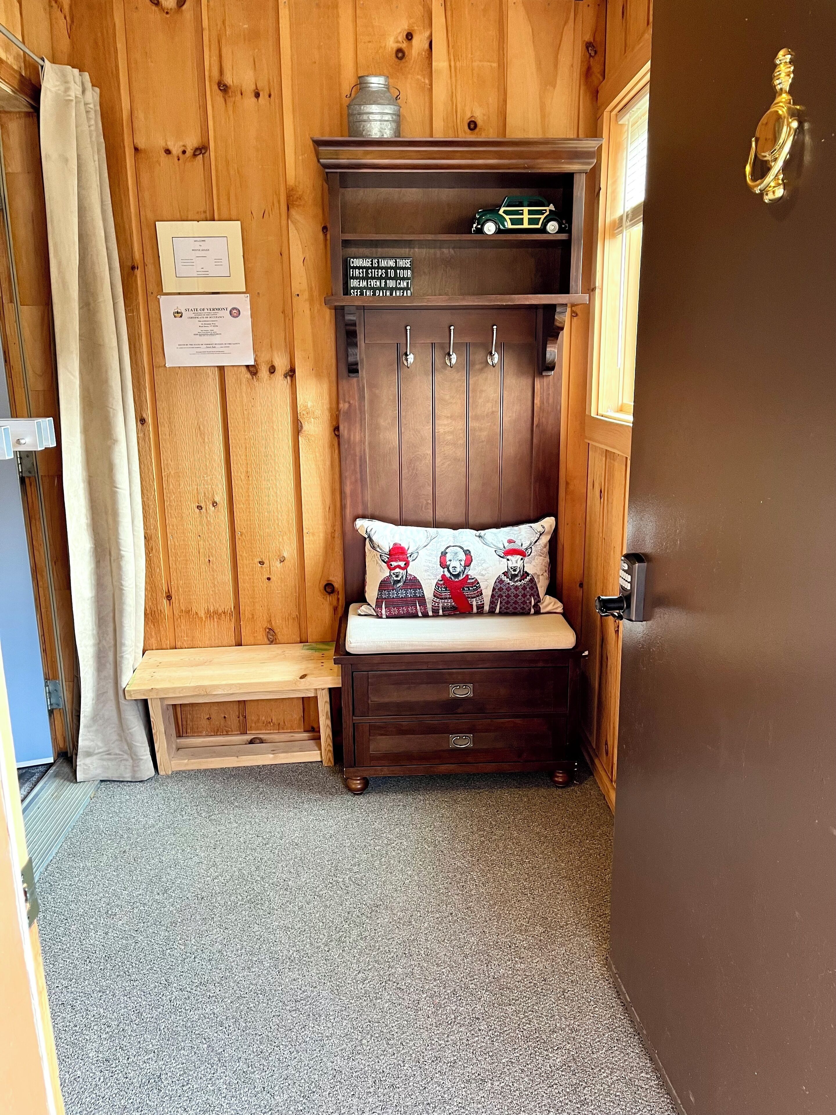 A small, cozy room with wooden walls, a bench, a cabinet with hooks, and a door with a brass handle.
