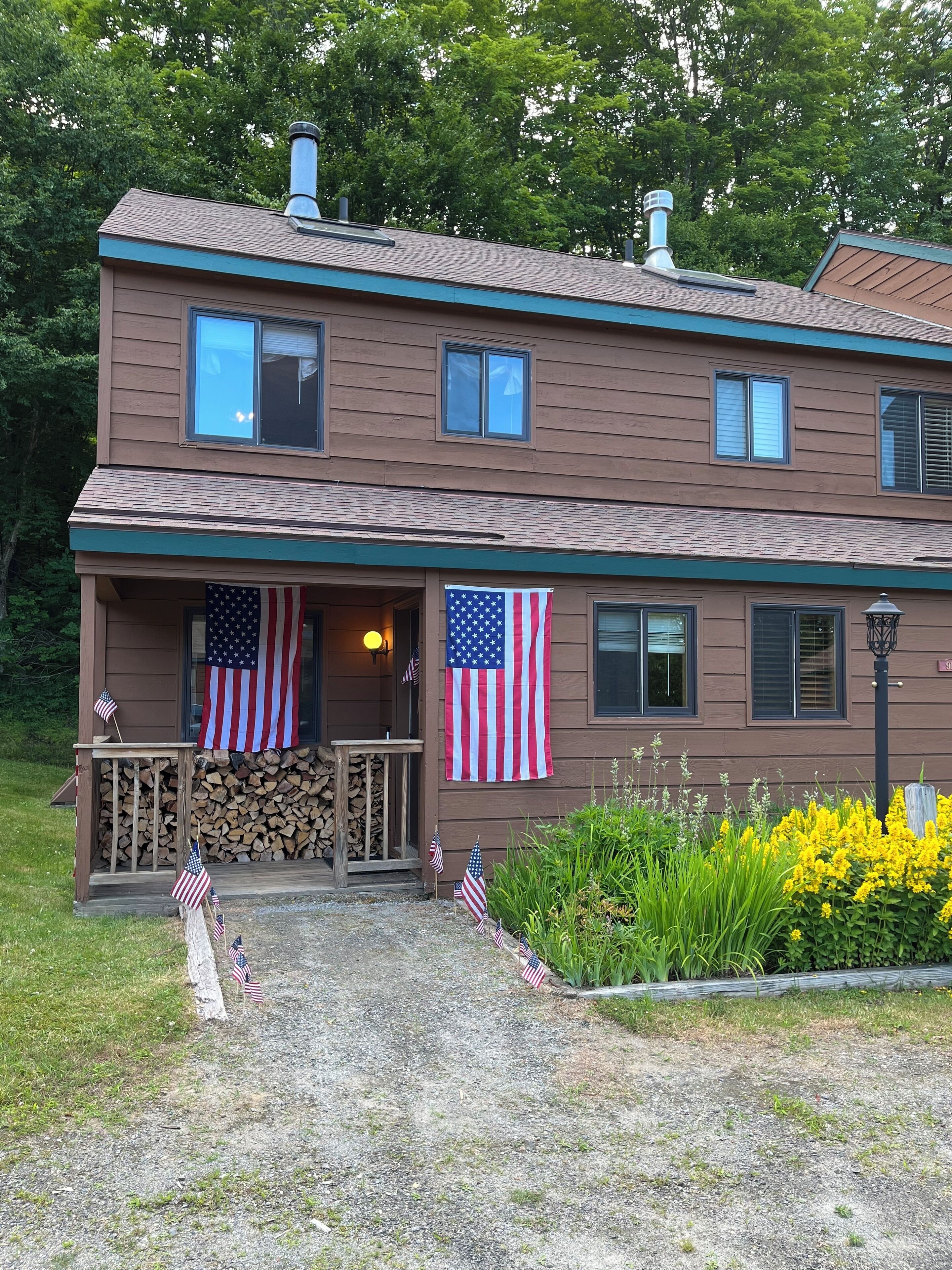 A two-story building with a porch, American flags, and a stack of firewood.