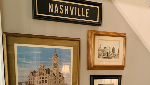 A staircase with a black handrail and a wall with framed pictures of buildings and a sign that reads "NASHVILLE". - Near Nashville Medical District (NASHVILLE)