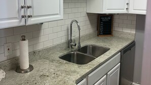 A kitchen with white cabinets, a granite countertop, a stainless steel sink, and a paper towel holder. - Near Nashville Medical District (NASHVILLE)