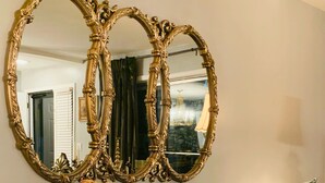 A green velvet sofa with tufted detailing and two pillows, a large ornate mirror above it, and a wooden side table. - Near Nashville Medical District (NASHVILLE)