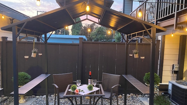 An outdoor patio with a pergola, two wicker chairs, a table with a glass, and a bottle.